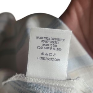 以下が含まれることがあります： 洗濯表示が記載された白いタグ。タグには「HAND WASH COLD WATER, DO NOT BLEACH, HANG TO DRY, COOL IRON IF NEEDED」と記載されています。ウェブサイトのアドレスFRANCESCAS.COMも印刷されています。