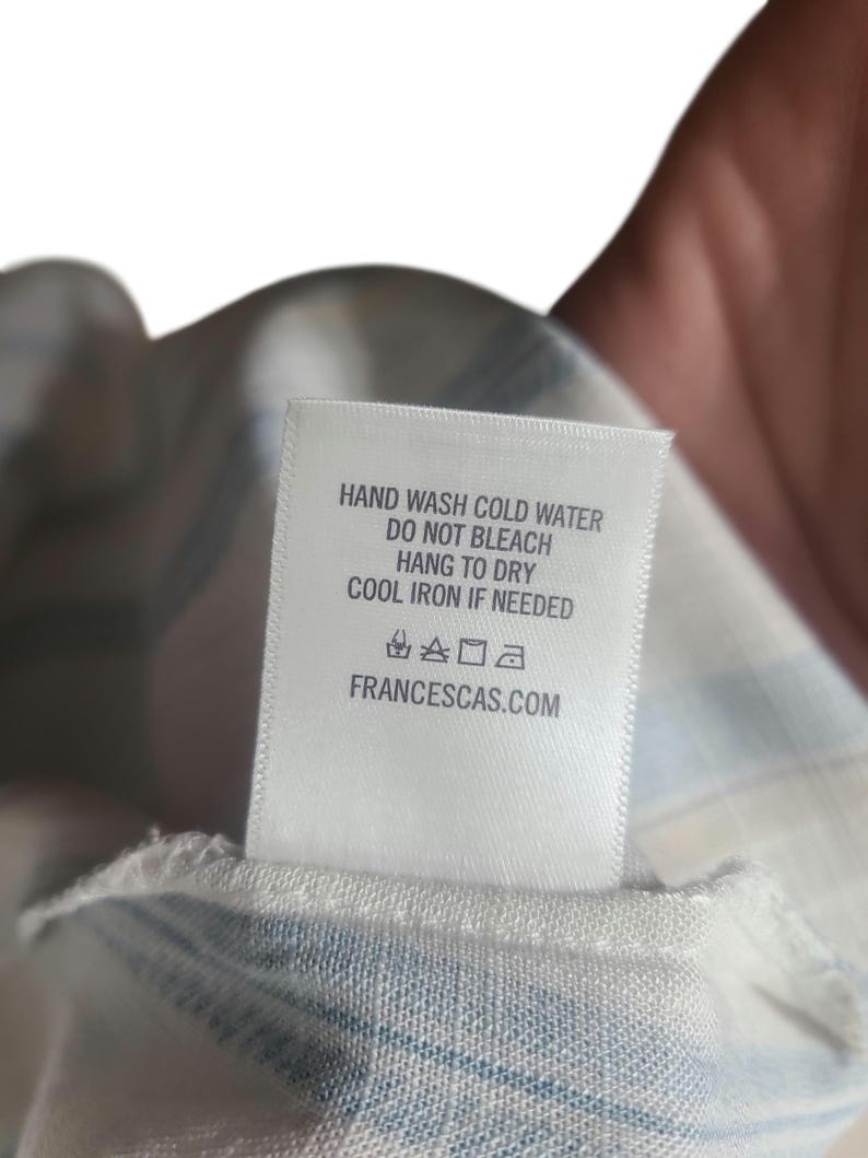 以下が含まれることがあります： 洗濯表示が記載された白いタグ。タグには「HAND WASH COLD WATER, DO NOT BLEACH, HANG TO DRY, COOL IRON IF NEEDED」と記載されています。ウェブサイトのアドレスFRANCESCAS.COMも印刷されています。