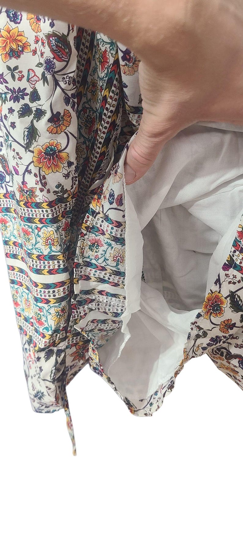 May include: A white dress with a floral pattern in yellow, orange, and purple. The dress has a white lining and a decorative border with a repeating pattern. The fabric is lightweight and appears to be suitable for warm weather.