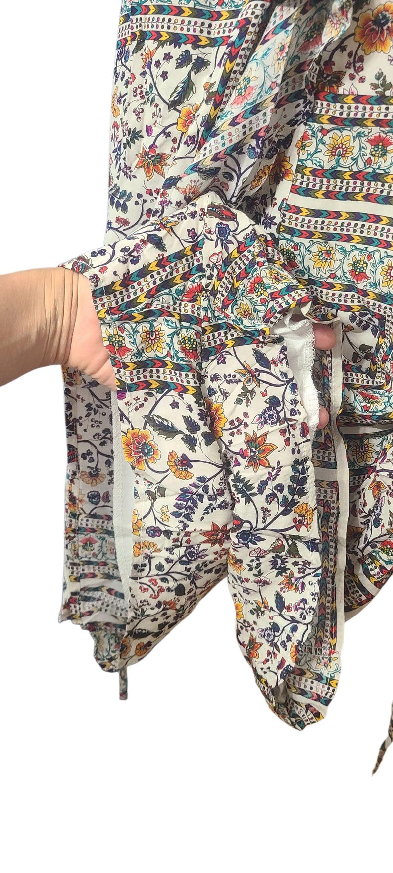 May include: Cream-colored fabric with a floral pattern in yellow, red, and blue. The fabric has a bohemian style with a mix of floral and geometric designs. The garment appears to be a top or dress.