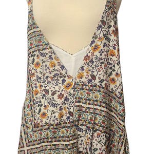 May include: A floral print romper with a deep V-neck and spaghetti straps. The romper features a white background with a colorful floral pattern in yellow, red, and blue. The garment is displayed on a mannequin.