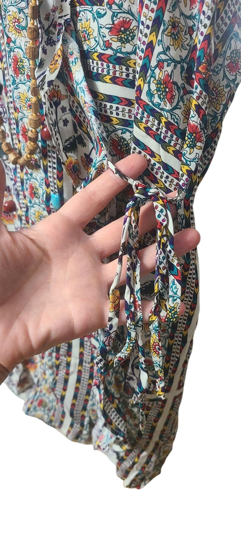 May include: A colorful, patterned tunic top with a floral and geometric design. The top features a mix of red, yellow, and blue flowers on a white background. The sleeves are visible, and the top has tie details.