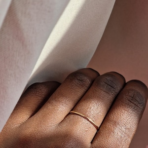 May include: A thin gold band ring worn on a person's finger.