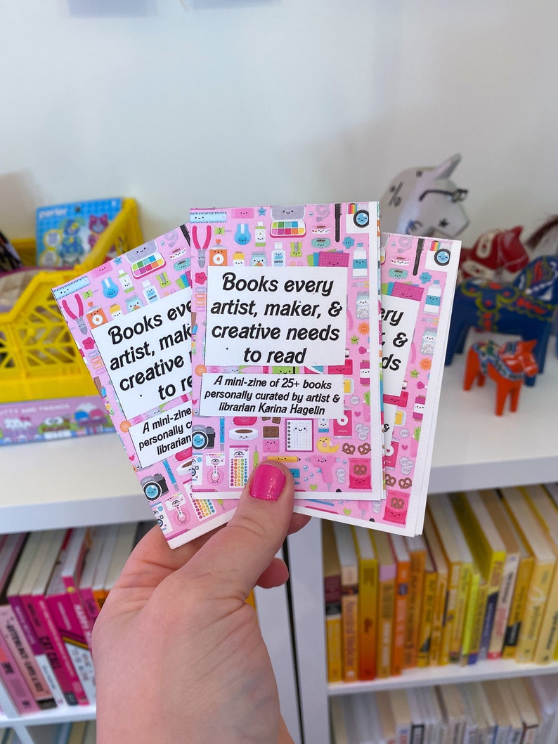 May include: Three pink mini-zines with a colorful pattern of illustrations. The text on the front reads "Books every artist, maker, & creative needs to read. A mini-zine of 25+ books personally curated by artist & librarian Karina Hagelin."