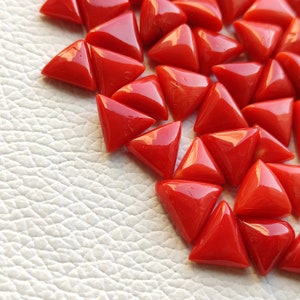 May include: A collection of triangular red coral gemstones. The coral is polished and has a glossy finish.