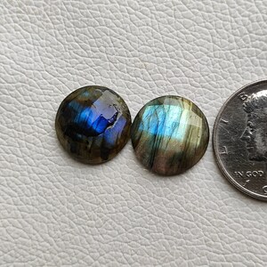 Può includere: Due pietre rotonde di labradorite iridescente con un bagliore blu e verde. Le pietre sono circa delle dimensioni di una moneta da dieci centesimi di euro.
