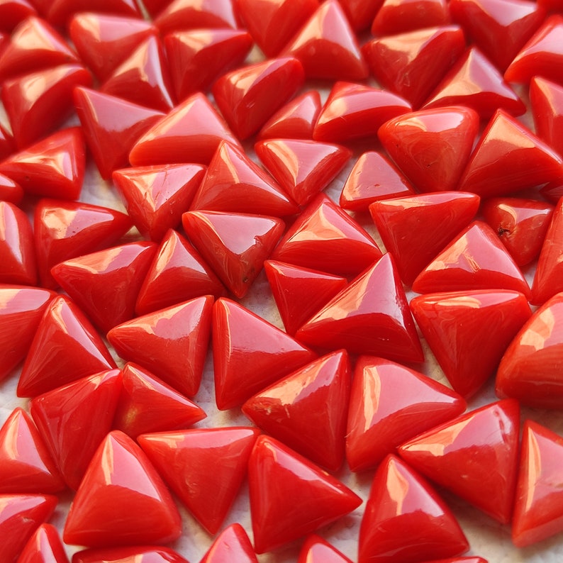 May include: A collection of triangular red coral gemstones. The coral is polished and has a glossy finish.