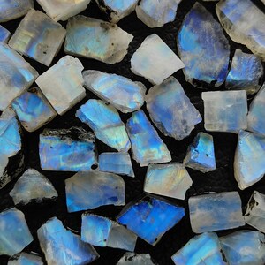 May include: A collection of iridescent blue and white moonstone chips. The chips are various sizes and shapes, with a natural, rough texture.