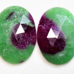 May include: Two oval-shaped gemstones with a green and purple color pattern. The gemstones have a faceted cut and are set in a bezel setting.