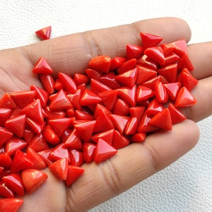 May include: A large pile of bright red triangular coral gemstones. The gemstones are smooth and polished, and they are arranged in a random pattern.