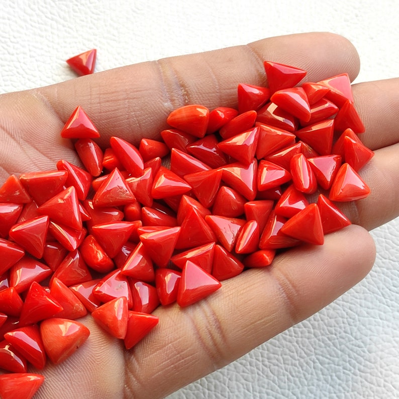 May include: A large pile of bright red triangular coral gemstones. The gemstones are smooth and polished, and they are arranged in a random pattern.