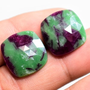 May include: Two green and purple gemstone cabochons with a faceted cut. The stones are square shaped and have a green and purple color.