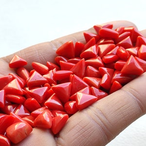 May include: A pile of bright red triangular coral beads. The beads are smooth and polished, and they have a natural, organic look.