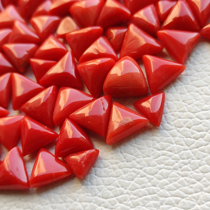 May include: A collection of triangular red coral gemstones. The coral is polished and has a smooth, glossy finish.