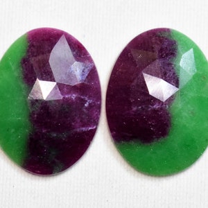May include: Two oval-shaped gemstones with a green and purple color pattern. The gemstones have a faceted cut and are set in a bezel setting.