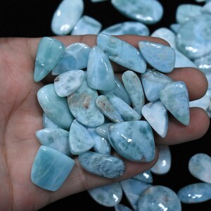 Puede incluir: Una colección de cabujones de piedras preciosas de color azul claro y blanco, con una variedad de formas y tamaños. Los cabujones son lisos y pulidos, con una apariencia translúcida.
