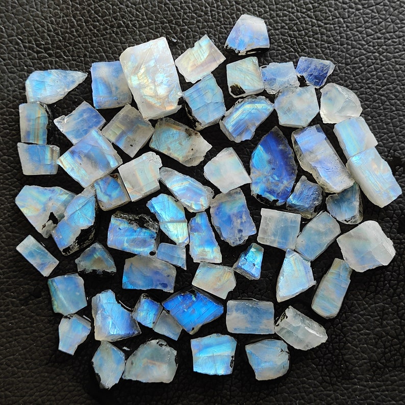 May include: A collection of iridescent blue and white moonstone chips. The chips are various sizes and shapes, with a natural, rough texture.