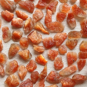 May include: A collection of rough, orange-brown sunstone crystals. The crystals are various sizes and shapes, with a shimmery, iridescent quality.