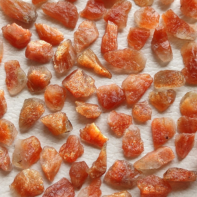 May include: A collection of rough, orange-brown sunstone crystals. The crystals are various sizes and shapes, with a shimmery, iridescent quality.