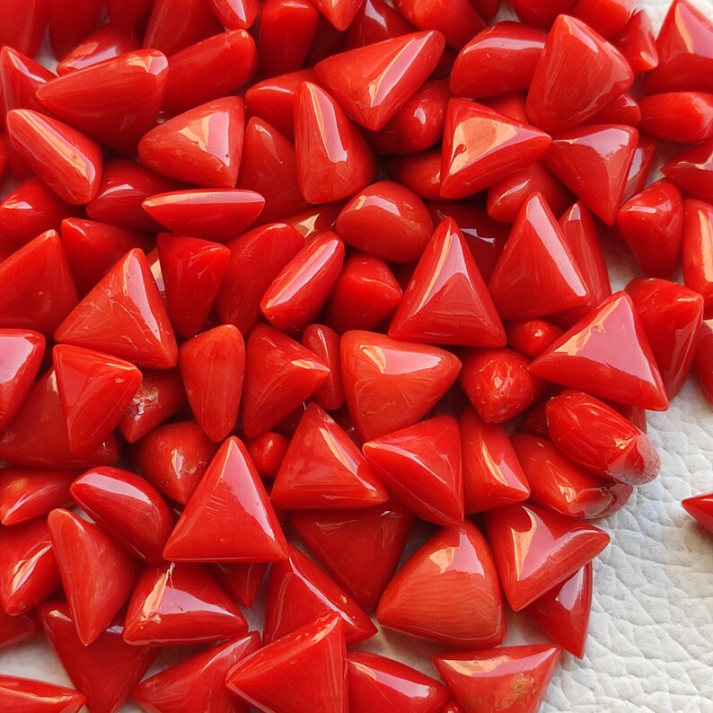 May include: A large pile of red coral triangle shaped beads. The beads are smooth and polished.
