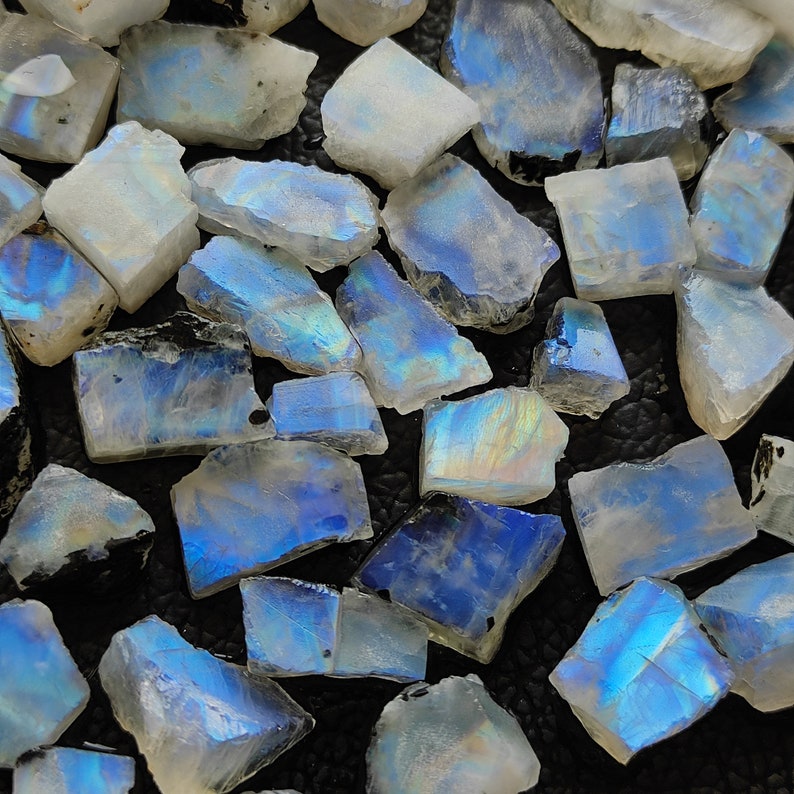May include: A collection of iridescent moonstone crystals in various shapes and sizes. The crystals are a light blue color with a shimmery, iridescent sheen.