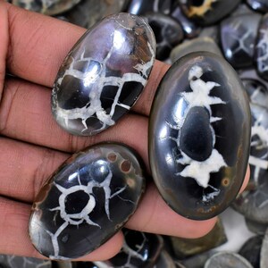May include: Three oval-shaped, polished, black and white agate cabochons with a unique, dendritic pattern. The cabochons are smooth and have a glossy finish.