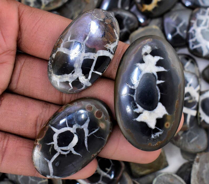 May include: Three oval-shaped, polished, black and white agate cabochons with a unique, dendritic pattern. The cabochons are smooth and have a glossy finish.