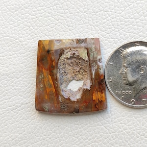 May include: A brown, orange and white agate cabochon with a hole in the centre. The cabochon is about the size of a UK 20 pence coin.