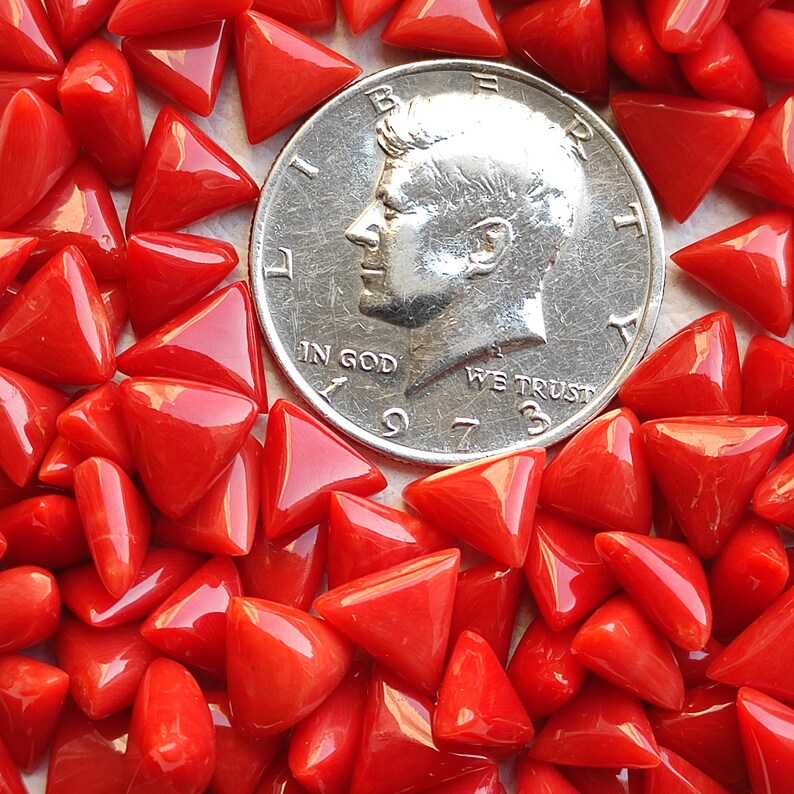May include: A close-up image of a pile of red triangular glass tiles. The tiles are scattered around a US quarter coin, showing their size and shape.