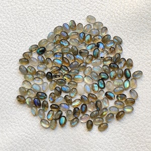 May include: A large group of oval-shaped labradorite gemstones in shades of gray, blue, and green. The stones have a iridescent sheen.