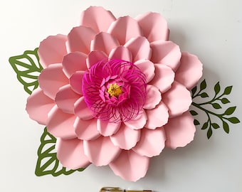 May include: A large pink paper flower with a smaller pink and yellow flower in the center. The flower is surrounded by green paper leaves.