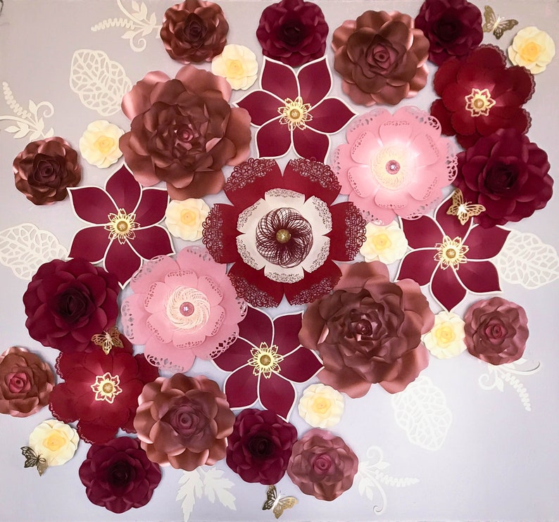 K&ouml;nnte beinhalten: Eine Sammlung von Papierblumen in den Farben Rosa, Rot und Wei&szlig;. Die Blumen sind in einem Kreis auf einem hellgrauen Hintergrund angeordnet.