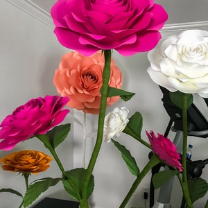 May include: A bouquet of large paper flowers in various colors, including pink, white, orange, and peach. The flowers are arranged in a vase and are displayed on a table.
