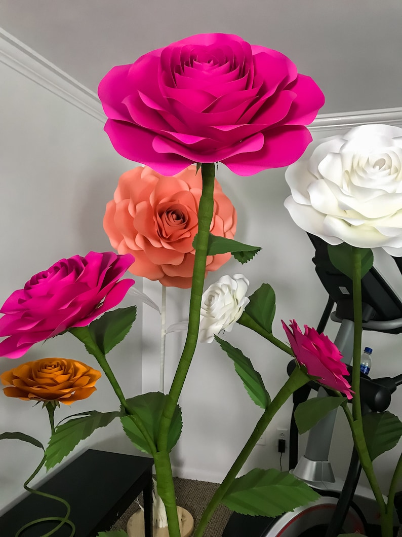 May include: A bouquet of large paper flowers in various colors, including pink, white, orange, and peach. The flowers are arranged in a vase and are displayed on a table.