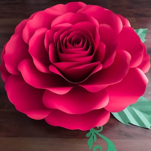May include: A large, bright pink paper rose with a layered center. The rose is surrounded by green paper leaves and a decorative swirl.