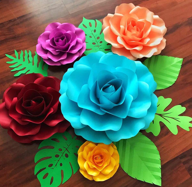 May include: A set of six paper flowers in various colors, including red, pink, orange, blue, and yellow. The flowers are surrounded by green paper leaves.