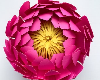 May include: A large, pink paper flower with a yellow center. The flower is made of many individual petals that are layered to create a 3D effect.