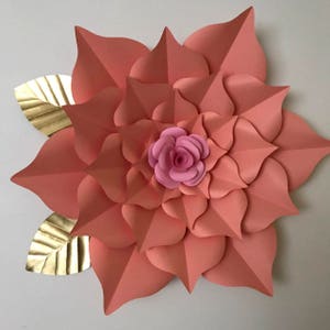 May include: A large, peach-colored paper flower with a smaller pink paper flower in the center. The flower is surrounded by two gold paper leaves.