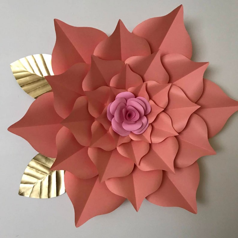 May include: A large, peach-colored paper flower with a smaller pink paper flower in the center. The flower is surrounded by two gold paper leaves.