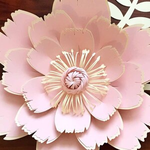 Puede incluir: Una gran flor de papel rosa con un diseño en capas y con volantes. El centro de la flor es una flor de papel rosa más pequeña con un centro amarillo.