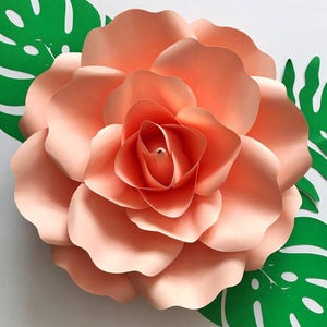 May include: A large, peach-colored paper flower with multiple layers of petals. The flower is surrounded by green paper leaves.