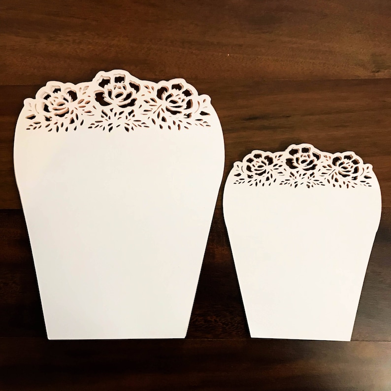 K&ouml;nnte beinhalten: Zwei wei&szlig;e Papierkegel mit einem zarten floralen Spitzenmuster. Die Kegel sind unterschiedlich gro&szlig;, wobei der gr&ouml;&szlig;ere Kegel h&ouml;her ist als der kleinere.