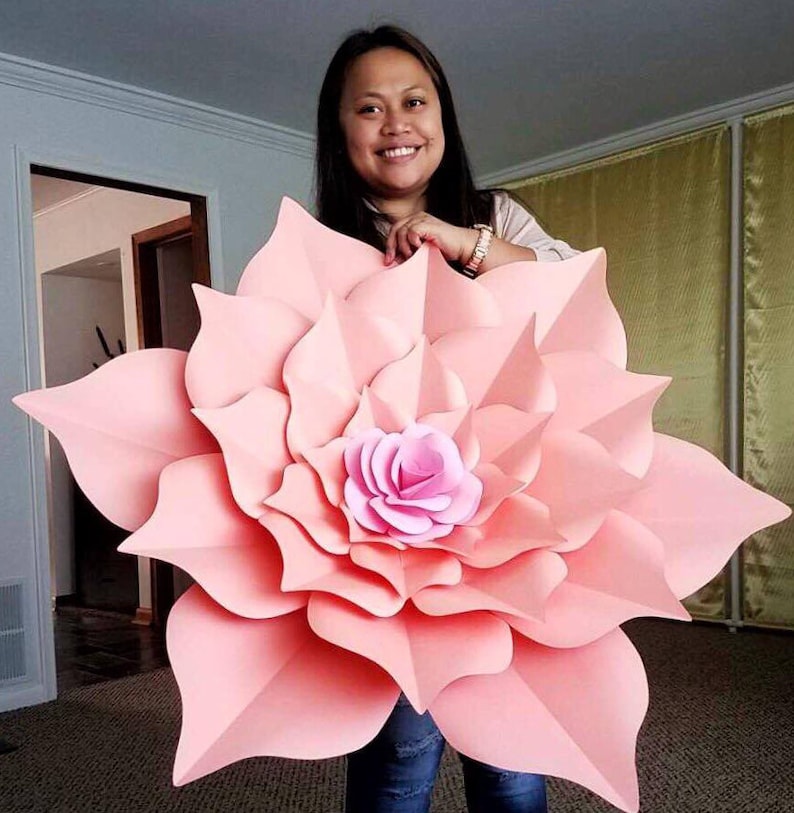 May include: A large, pink paper flower with a smaller pink flower in the center. The flower is made of multiple layers of paper and has a delicate, layered look.