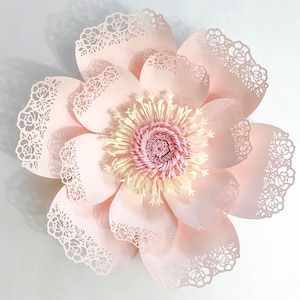 K&ouml;nnte beinhalten: Eine gro&szlig;e, rosafarbene Papierblume mit einem zarten Spitzenmuster an den R&auml;ndern. Die Mitte der Blume ist eine kleinere, rosafarbene und gelbe Papierblume.