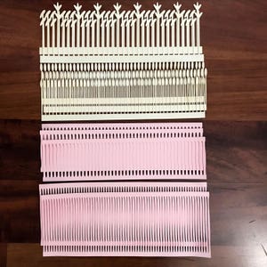 Puede incluir: Disposici&oacute;n de elementos de papel troquelado en crema y rosa. Las piezas de color crema tienen un borde superior decorativo y l&iacute;neas verticales. Las piezas rosas tienen un dise&ntilde;o similar a flecos. Estos recortes de papel son probablemente para manualidades o &aacute;lbumes de recortes.