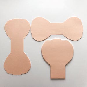May include: Three peach-colored paper shapes for crafting. The shapes are a bow, a circle with a rounded bottom, and a teardrop shape with a rounded bottom.