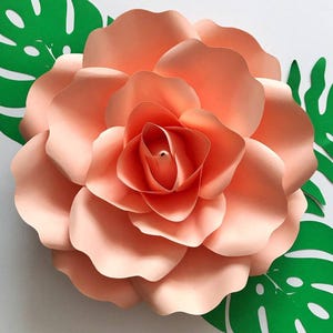 May include: A large, peach-colored paper flower with multiple layers of petals. The flower is surrounded by green paper leaves.