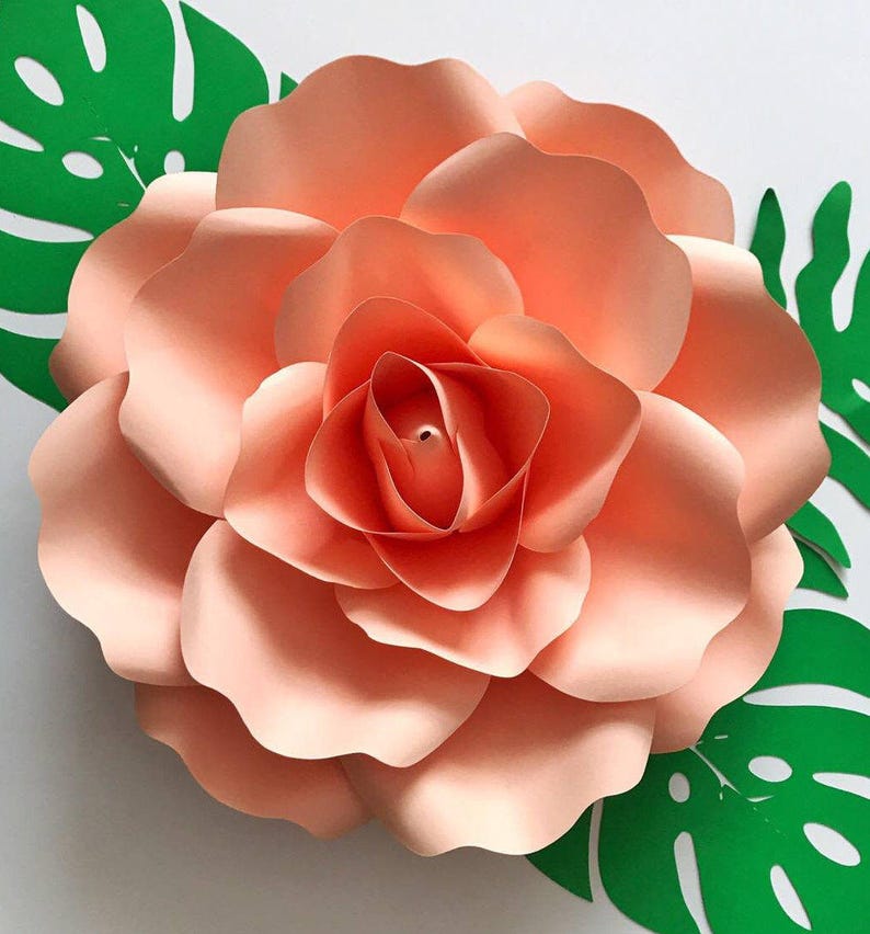 May include: A large, peach-colored paper flower with multiple layers of petals. The flower is surrounded by green paper leaves.