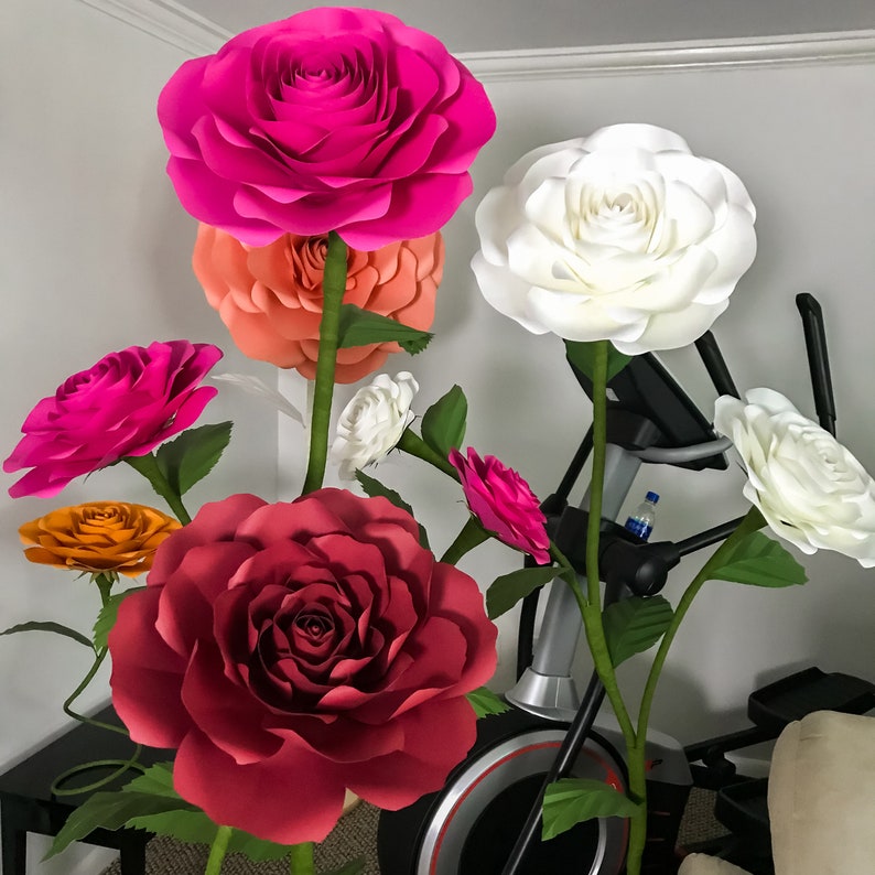 May include: A bouquet of paper flowers in various shades of pink, white, and orange. The flowers are arranged in a vase and are displayed on a table. The flowers are made of paper and have a realistic appearance.