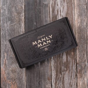 May include: A black box with a wood grain pattern and the text "quality gifts MANLY MAN COMPANY" in gold lettering.